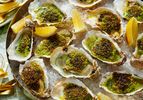Roasted oysters topped with herbs and seasoning arranged on a platter with lemon wedges
