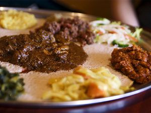 A large injera-lined platter topped with various Ethiopian dishes, many of which are flavored with niter kibbeh.