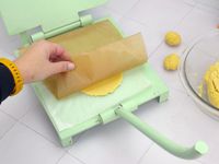 a person peeling off the liner from a tortilla in the press