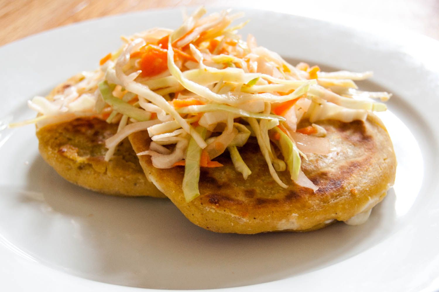 Two Salvadoran pupusas on a plate, topped with curtido, a type of slaw. 