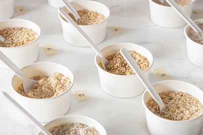 Multiple small cups each containing oatmeal arranged on a surface with plastic spoons and small numbered labels