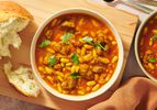 2 bowls of Loubia Stew on a wooden board with bread on the side and fabric napkin on the bottom of photo