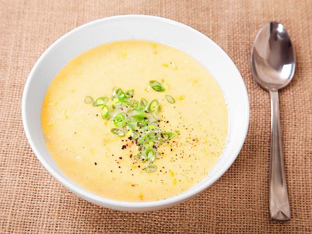 Overhead view of a bowl of finished corn chowder, garnished with scallion and ground black pepper.
