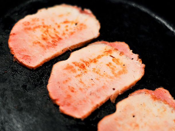 Three slices of Canadian bacon being panfried. 