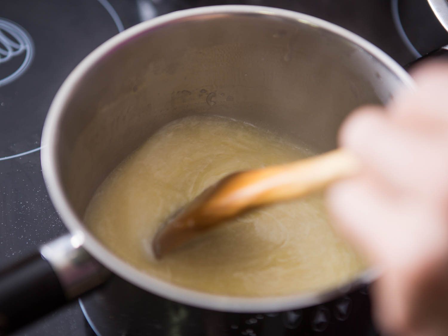 Stirring fondue with a wooden spoon.