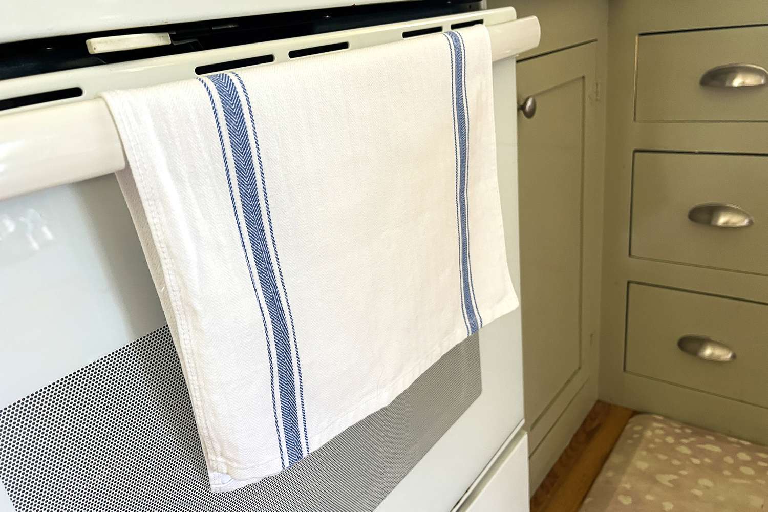 Kitchen oven door with a white towel featuring blue stripes draped over the handle
