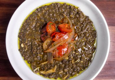 Overhead shot of a bowl of chicken and lentil stew topped with fried onions and tomatoes