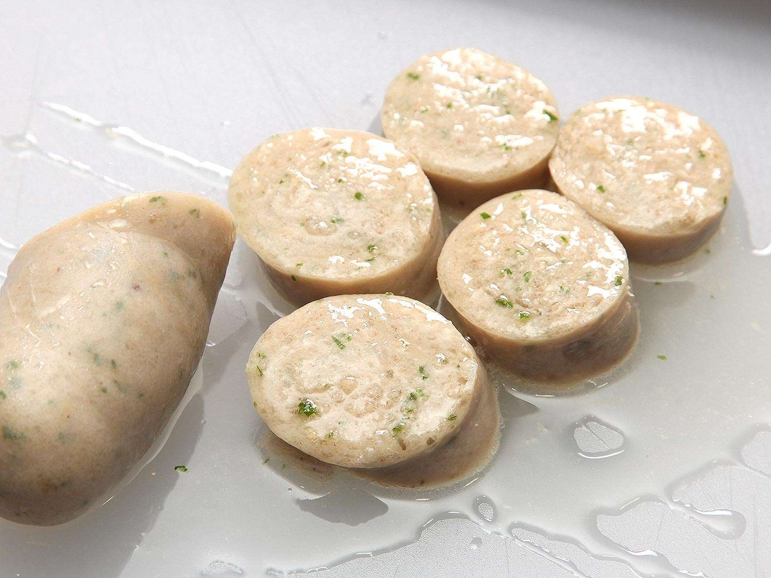 A sliced link of weisswurst made with 42% fat. The slices are glistening and fat has pooled on the cutting board underneath.