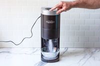 A person operating Hawaiian Shaved Ice HomePro Shave Ice and Snow Cone Machine (S777) with ice falling into a bowl