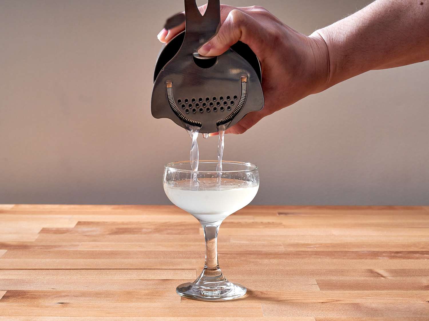 A cocktail being strained into a coupe glass