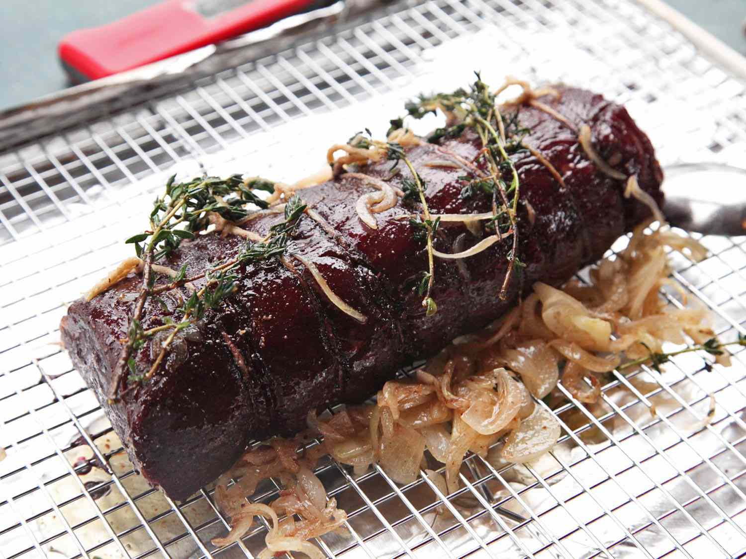 Beef tenderloin roast resting on bed of shallots on rack over baking sheet