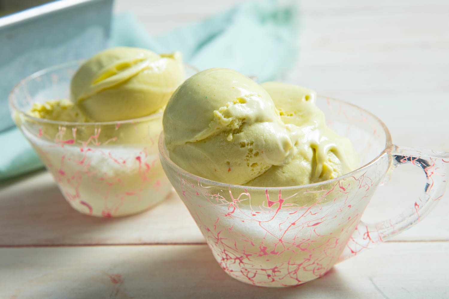 Two scoops of pistachio ice cream served in a glass teacup clouded by frost.