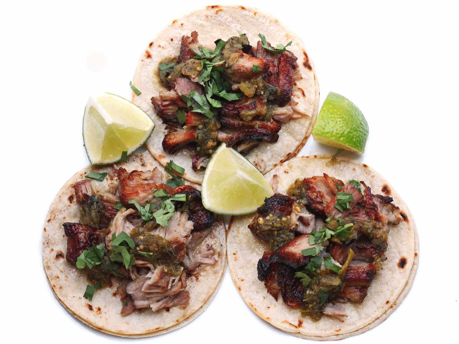 Three tacos topped with finished carnitas, salsa, and chopped cilantro, and garnished with quartered limes.