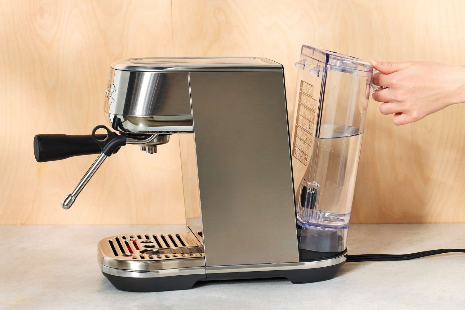 Hand attaching filled water tank from Breville Bambino Plus Espresso Machine on white countertop
