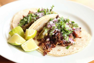 Carnitas tacos on a plate with lime wedges. 