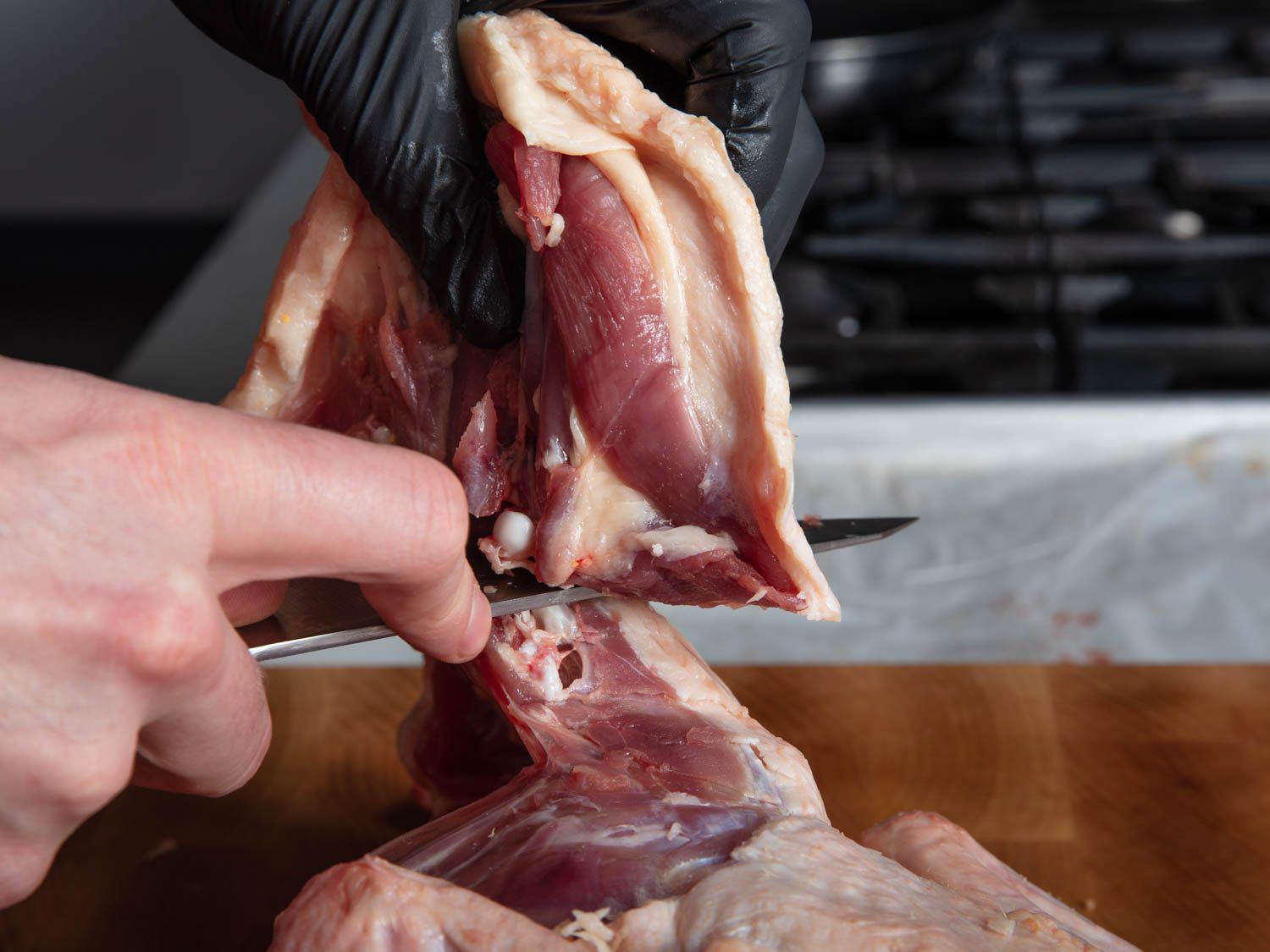 Closeup side view of cutting away a duck leg with a sharp knife.
