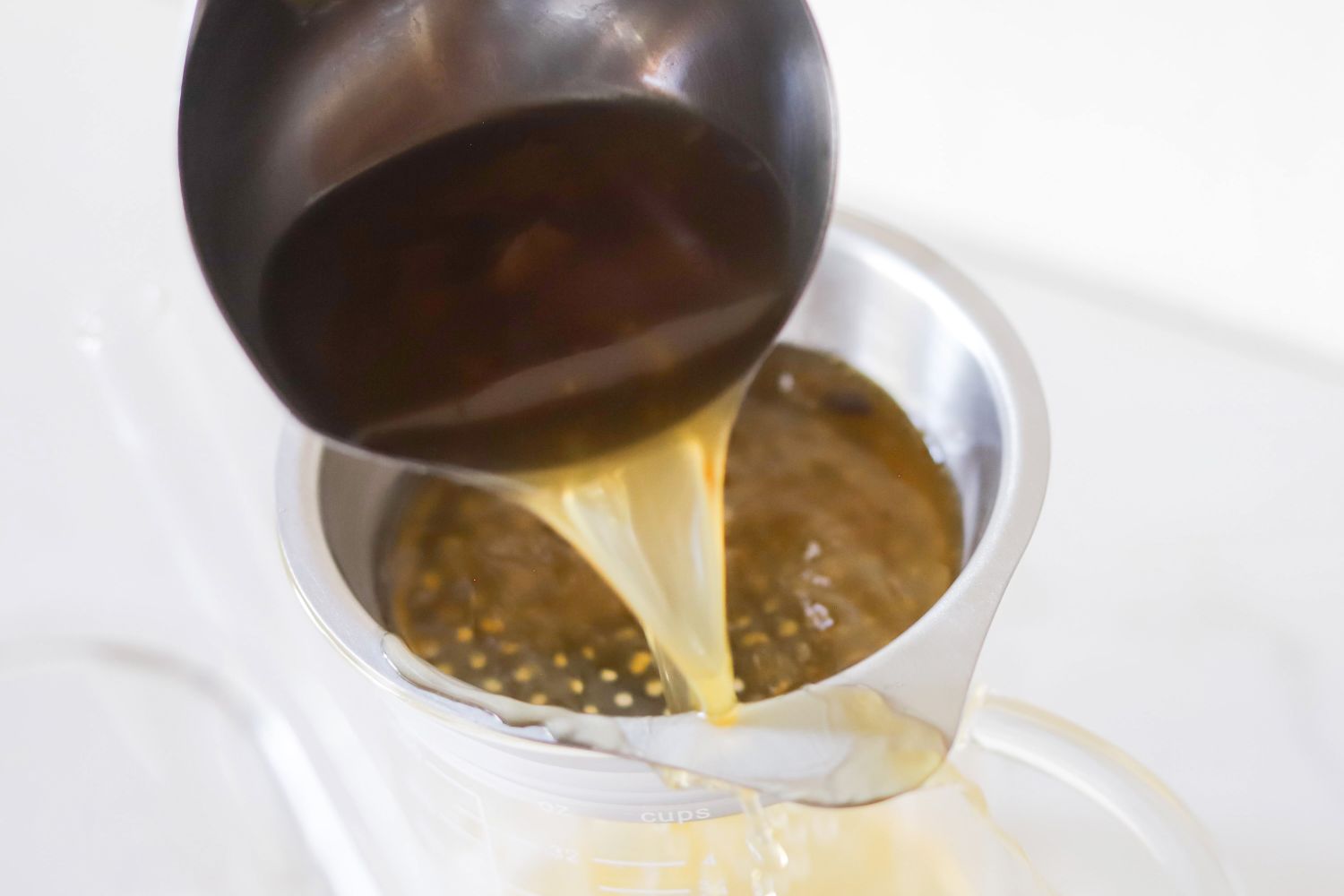 Broth being poured through the strainer of a fat separator