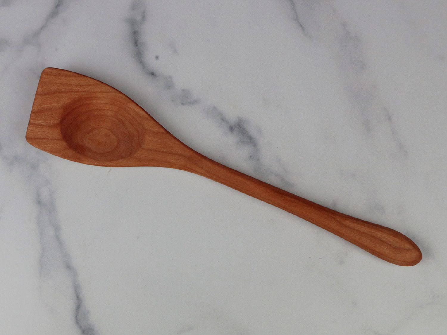 a wooden spoon with an angled head on a white marble backdrop
