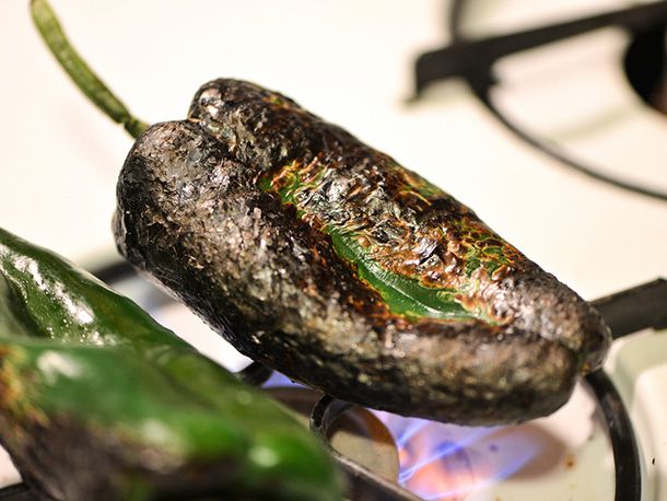 Poblano chiles are charred over a gas burner.