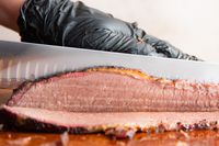 A person slicing meat using the Victorinox Fibrox Pro Slicing Knife