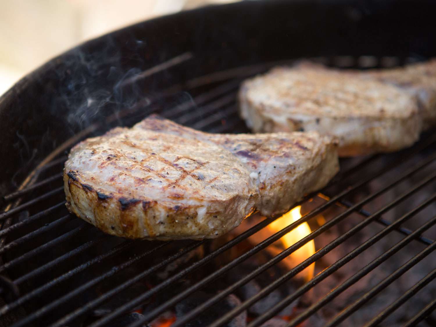 Pork chops cooking on a charcoal grill (one side has already been cooked with char marks).