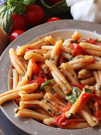 Finished dish of pasta with blistered cherry tomato sauce, next to a block of cheese, basil sprig, garlic, and tomatoes
