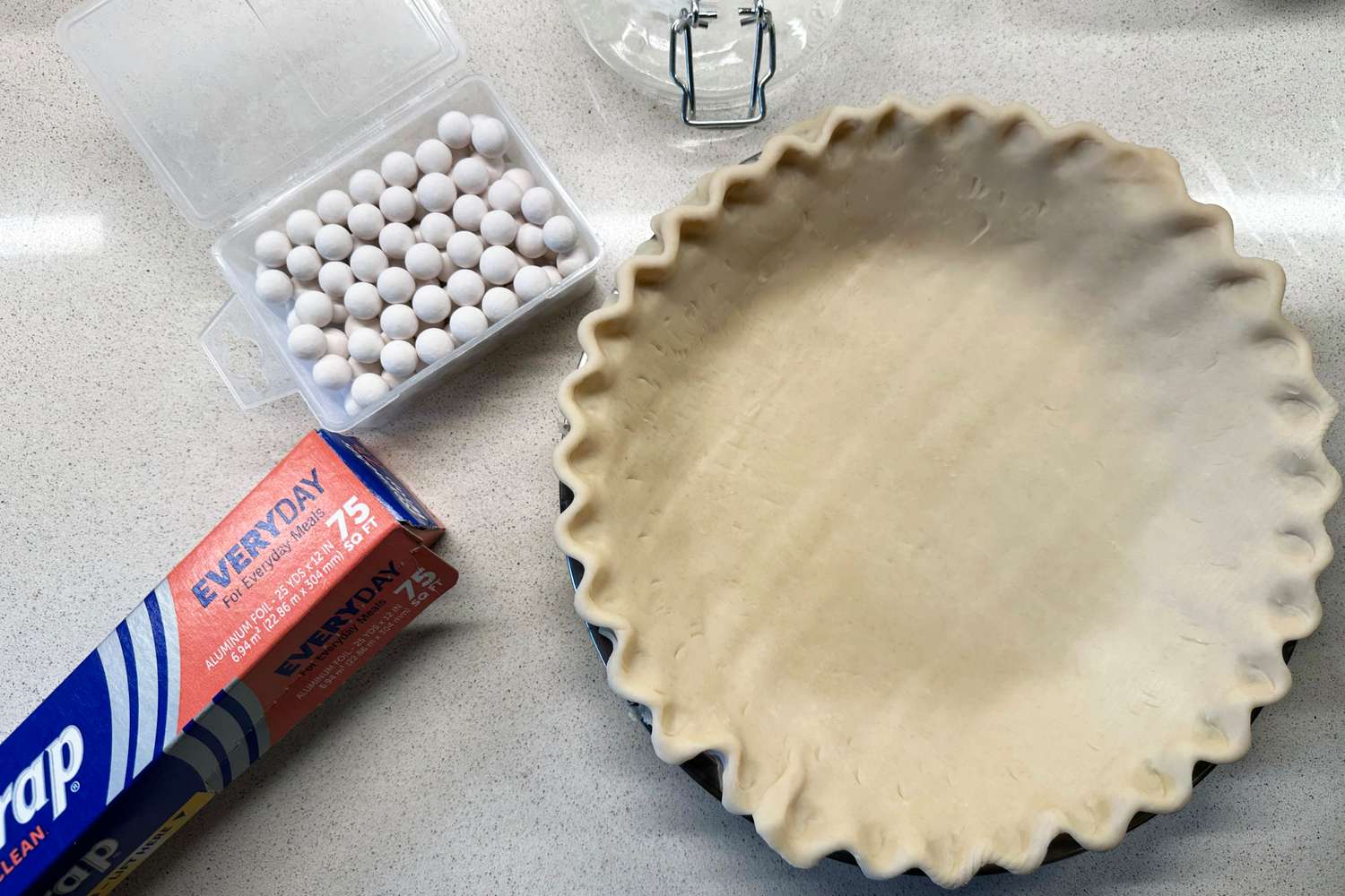 A box of ceramic pie weights next to a pie pan lined with raw dough.