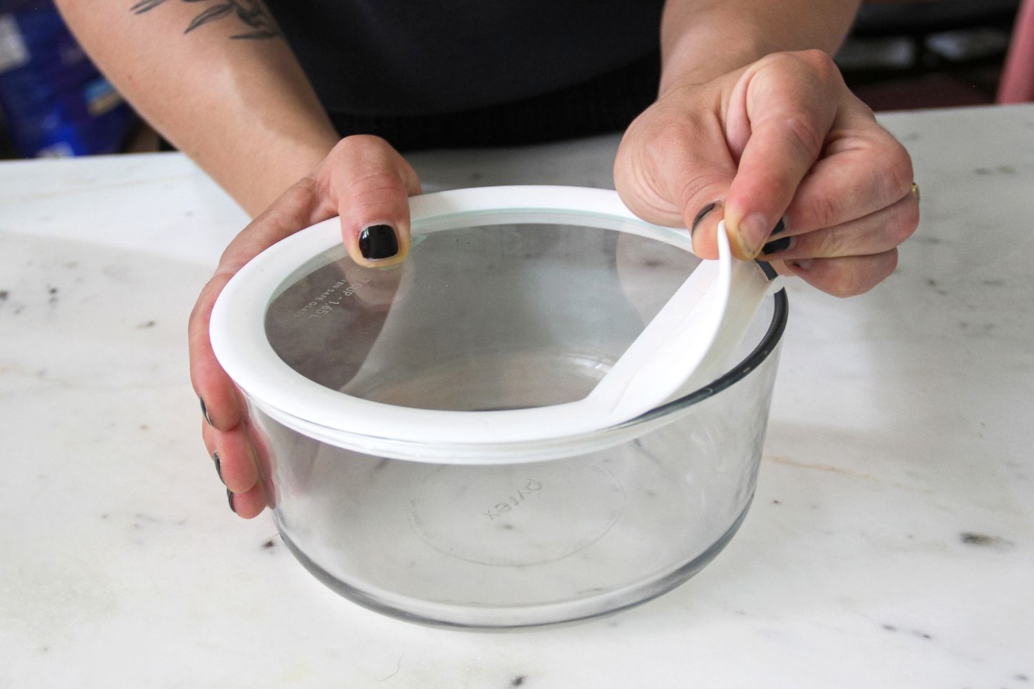 Hands holding a round glass container with a lid from Pyrex Ultimate 10-Piece Glass Storage Set demonstrating removal of the lids silicone seal