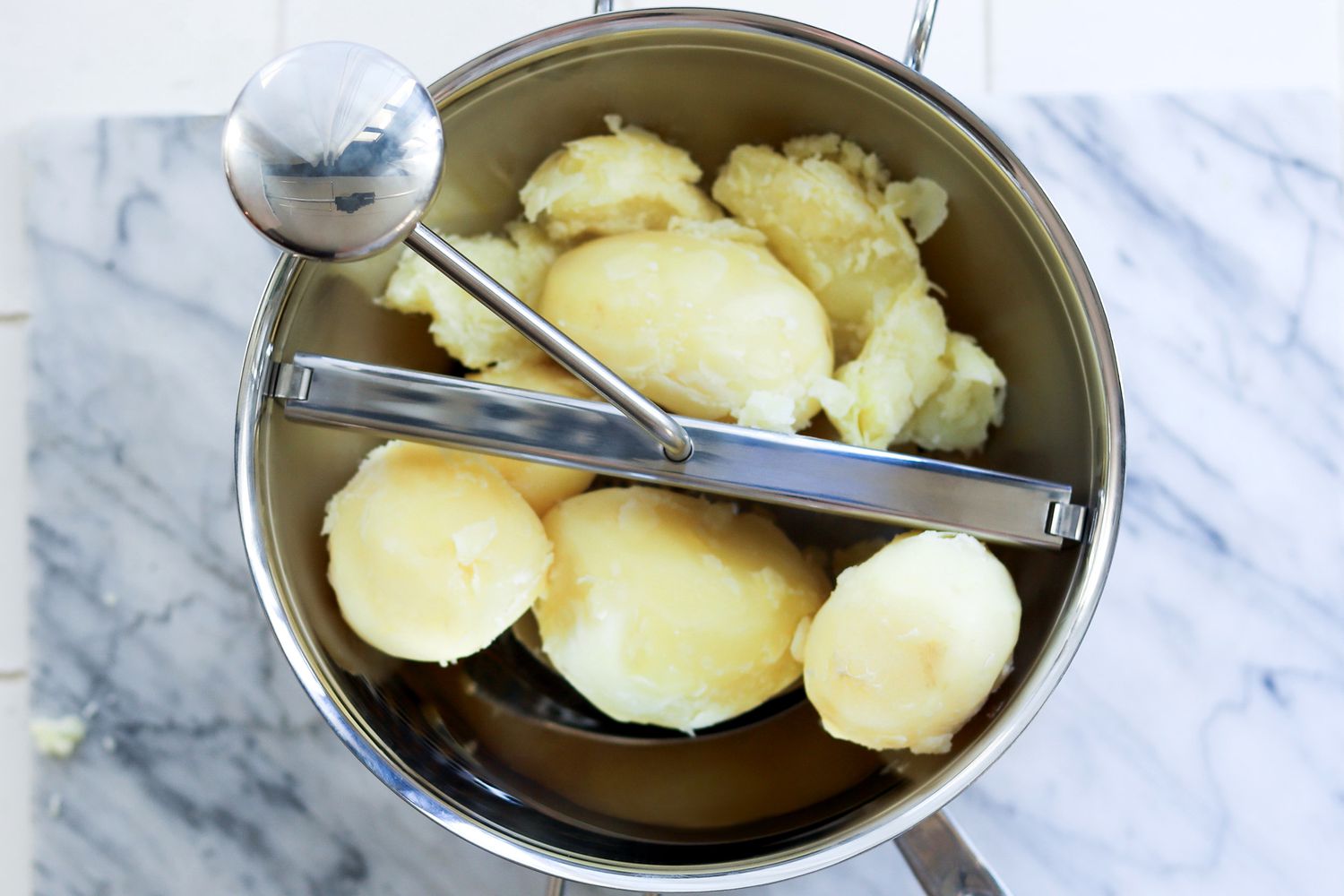 a food mill with boiled whole potatoes inside it