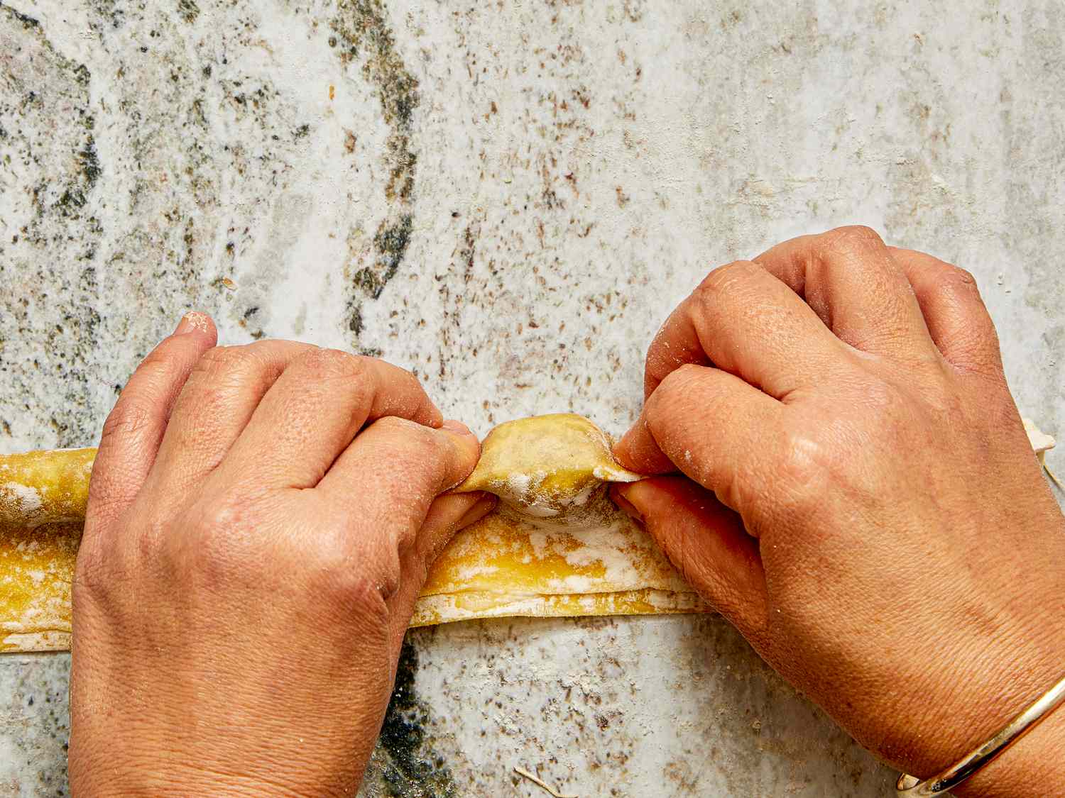 Hands shaping pasta on a countertop making agnolotti