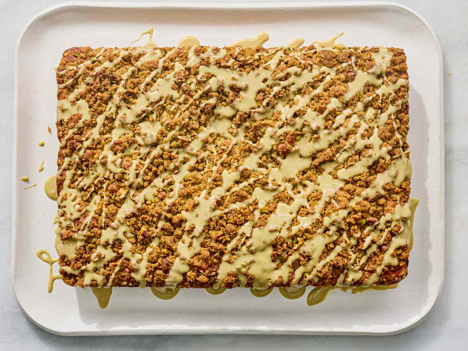 A rectangular coffee cake drizzled with glaze and topped with crumble on a white tray