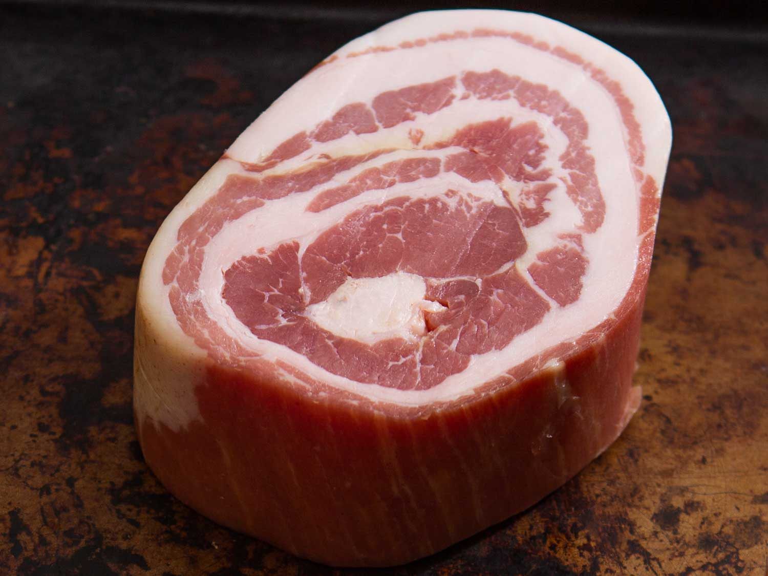 Thick slab of pancetta on a dark brown background.