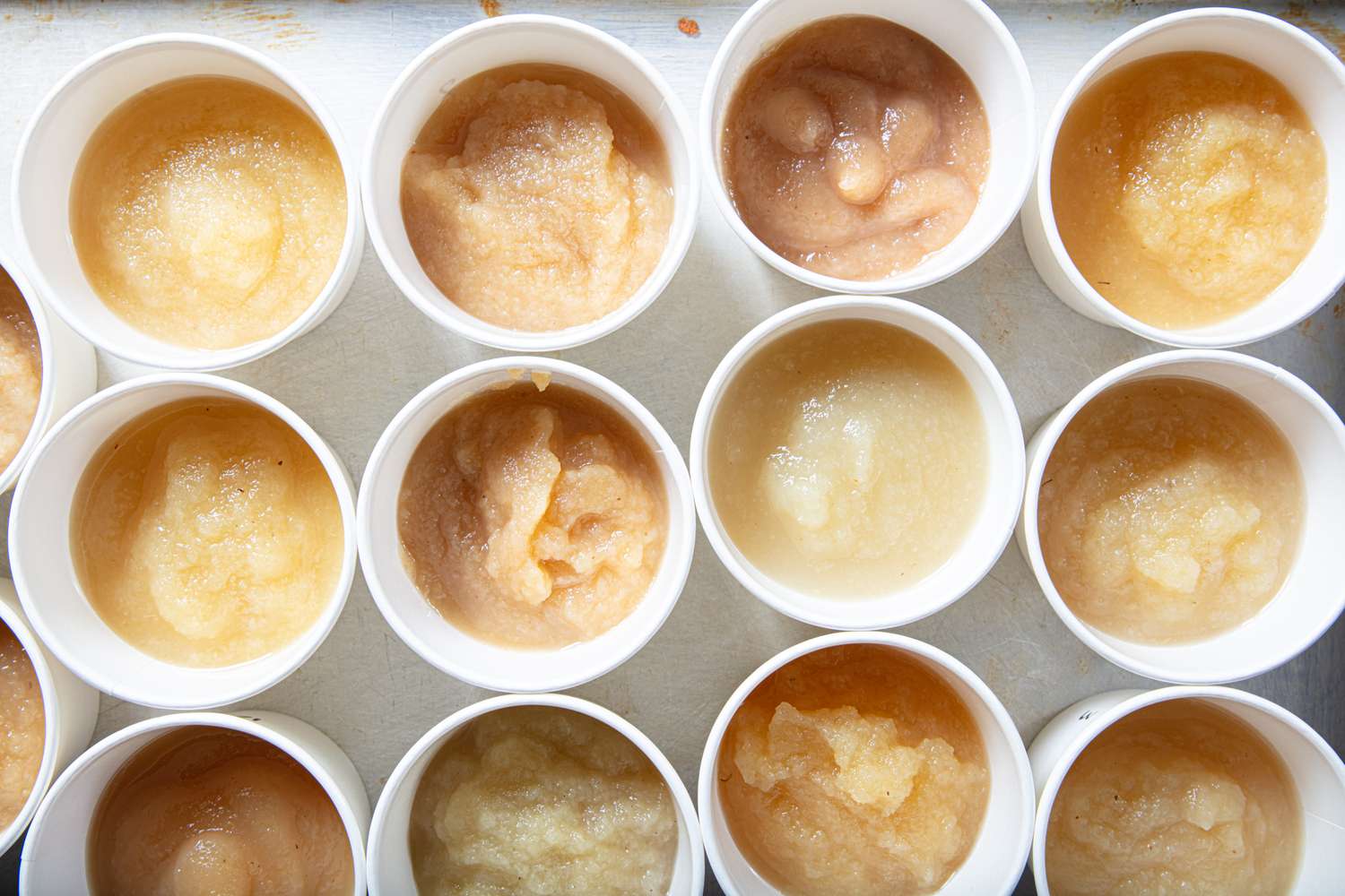 Assorted cups of applesauce displayed in rows on a surface