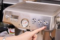 A person presses a button on the Breville BES920XL Dual Boiler Espresso Machine