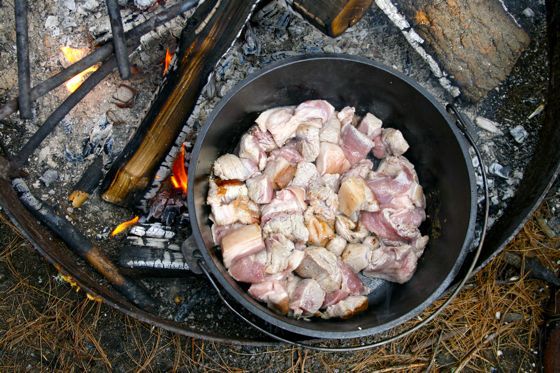 Starting to sear meat in a Dutch oven set over coals.