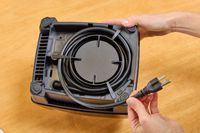 A hand holding the cord on the bottom of the Vitamix E310 Explorian Blender on a wooden background