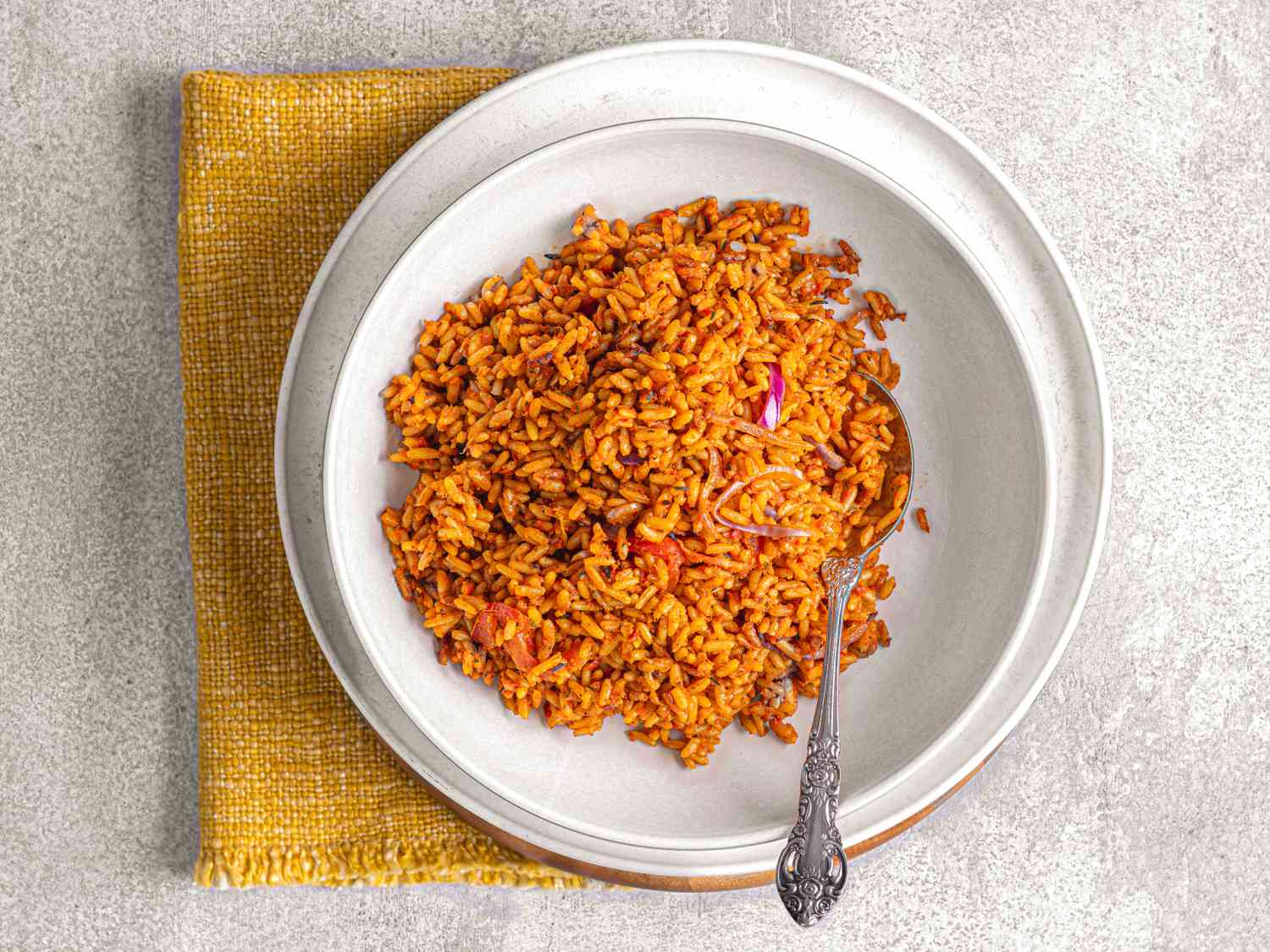 Overhead view of Jollof rice in a white bowl with a spoon