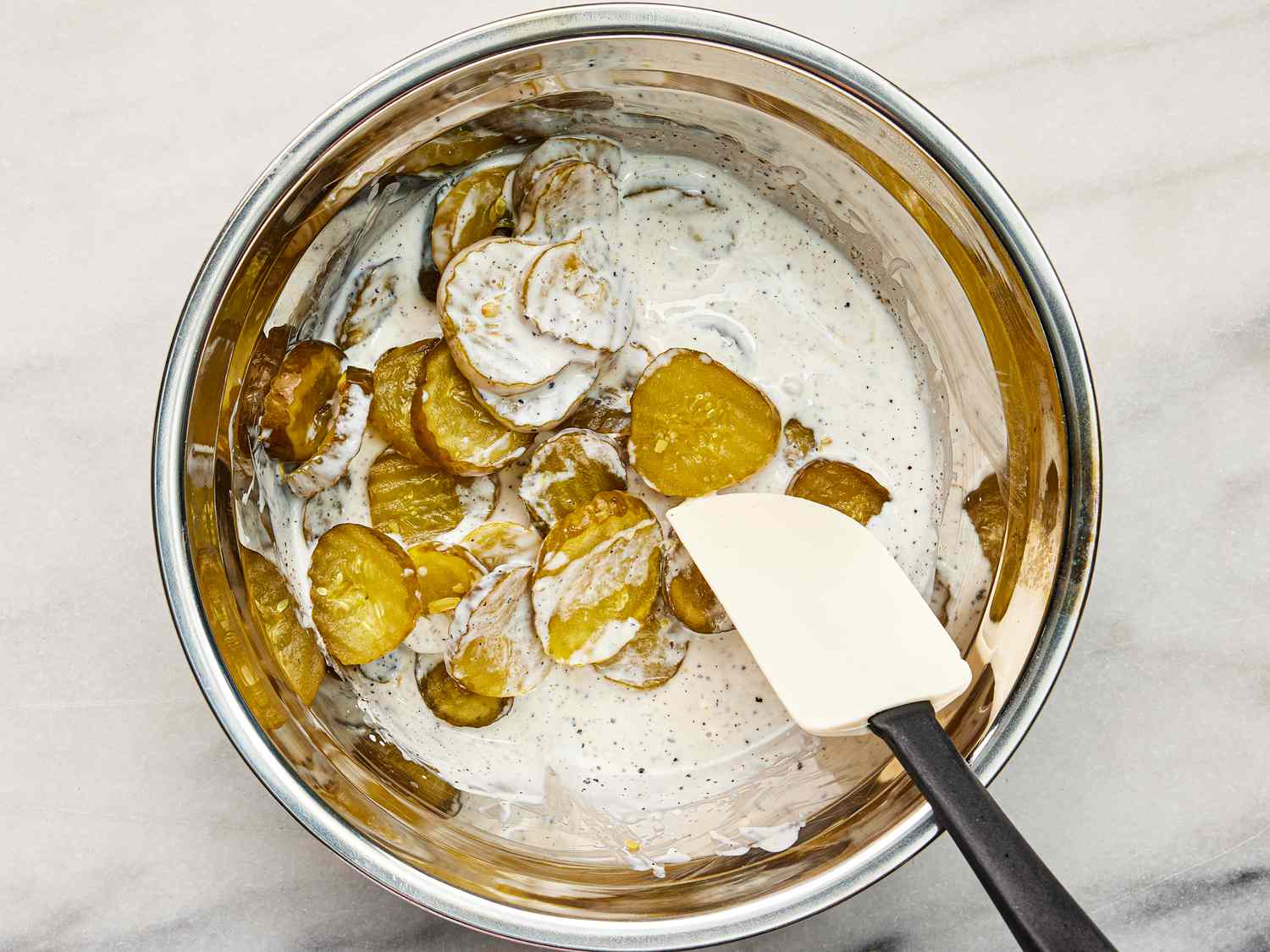 sliced pickles mixed into buttermilk mixture in bowl with spatula 