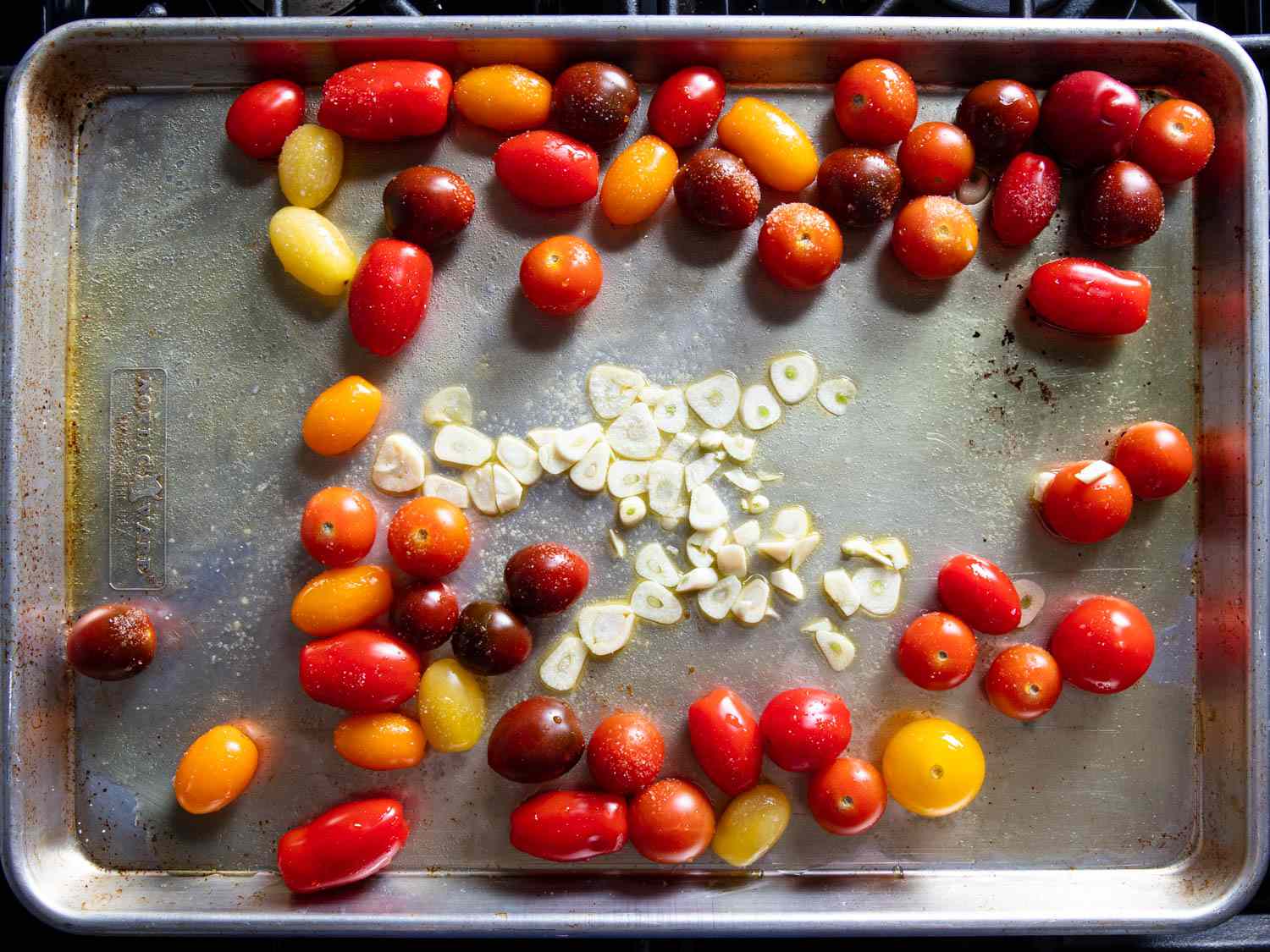 Cherry tomatoes and sliced garlic on a sheet pan