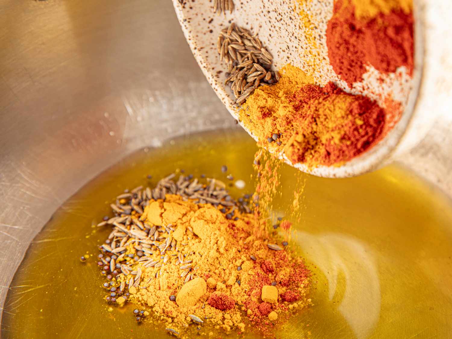 Spices being added to oil in a cooking pan