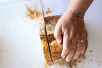 A hand with a ring slicing a loaf of bread on a white surface