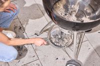 A person removing the bottom of the Weber Original Kettle Premium 22-Inch Charcoal Grill