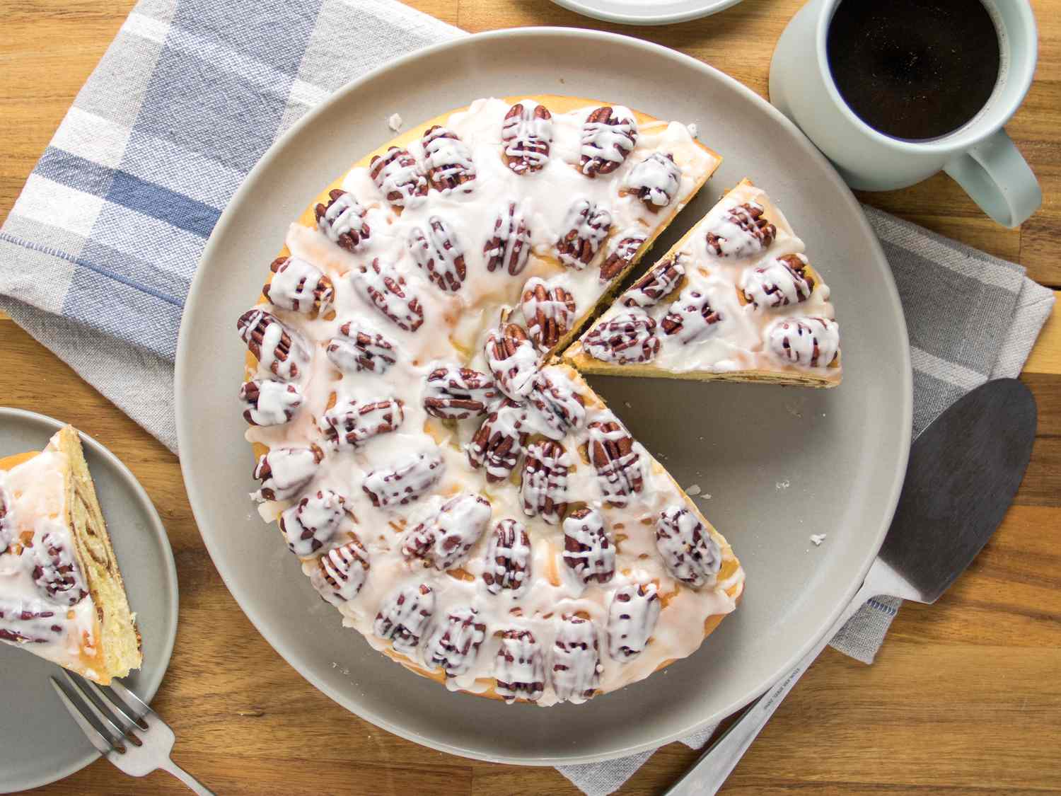 Yeasted coffee cake on wooden table with blue and white plaid napkin, cup of coffee and small plate