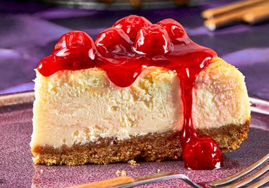 Slice of cheesecake topped with cherry topping on a plate with a fork nearby