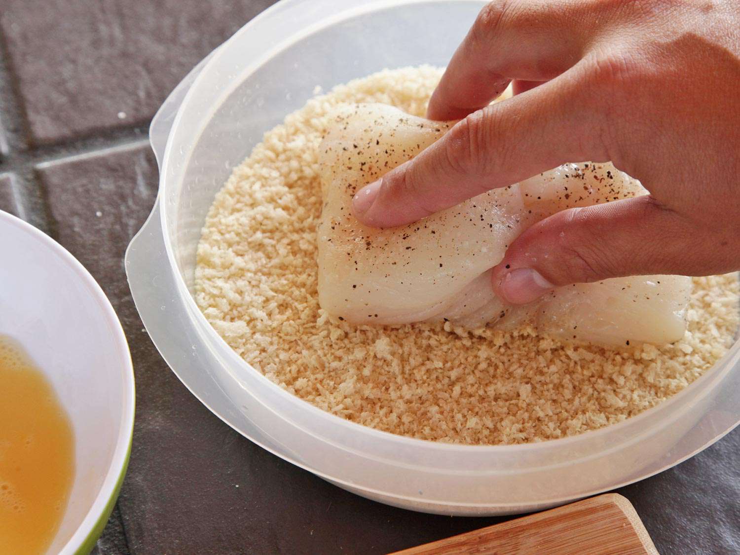 Pressing a fish fillet into a container of panko bread crumbs. 
