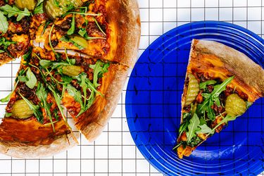 Slice of cheeseburger pizza on a blue plate. Rest of cheeseburger pizza on graphic background 