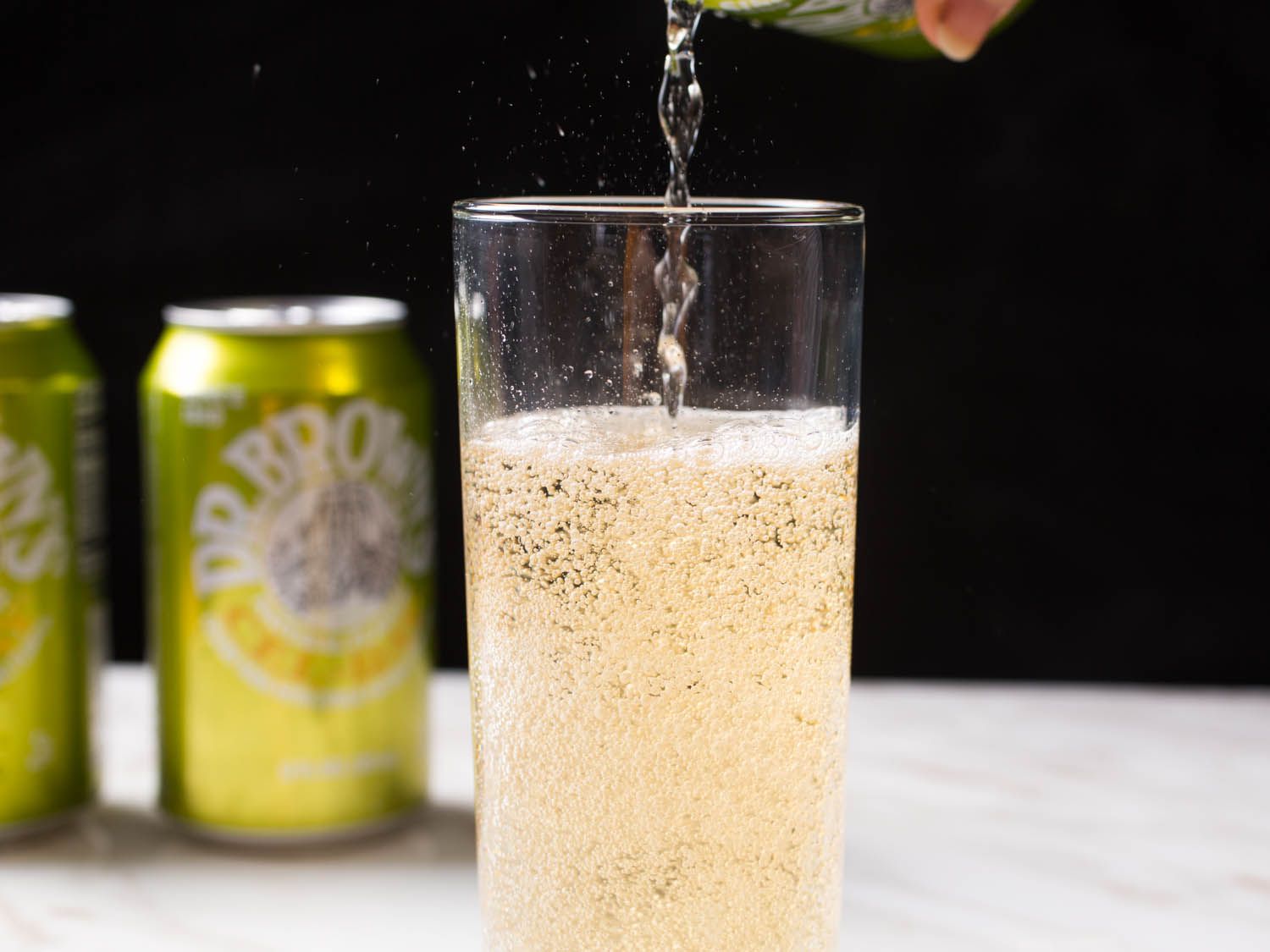 A tall glass mostly filled with Dr. Brown's Cel-Ray soda, with more being poured in from above.