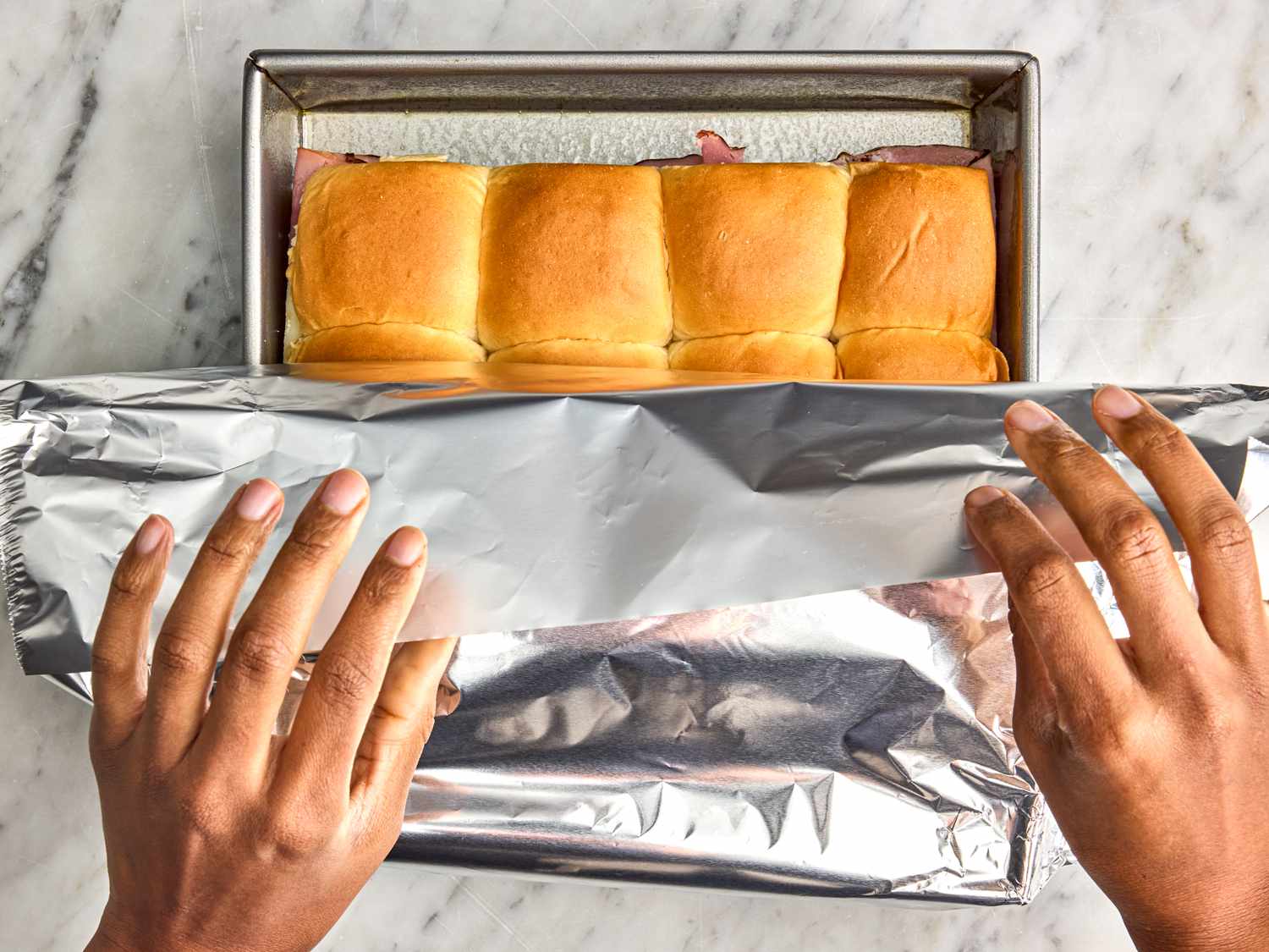 A person wrapping ham and cheese sliders in aluminum foil