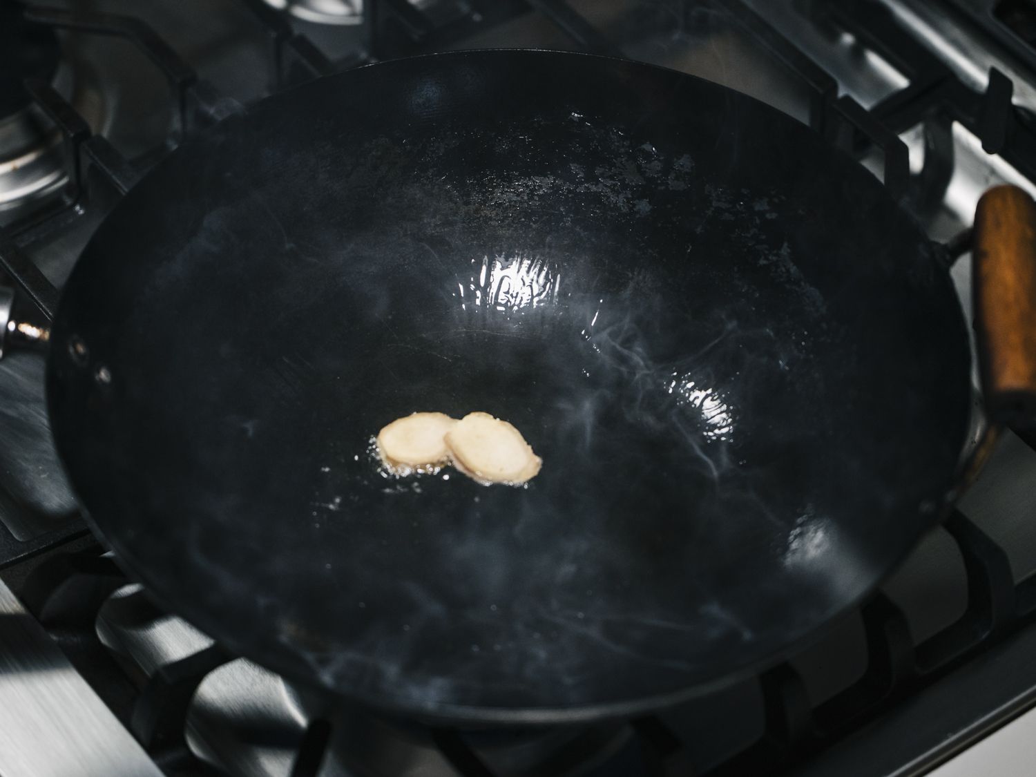 Two pieces of ginger sizzling in a smoking wok.
