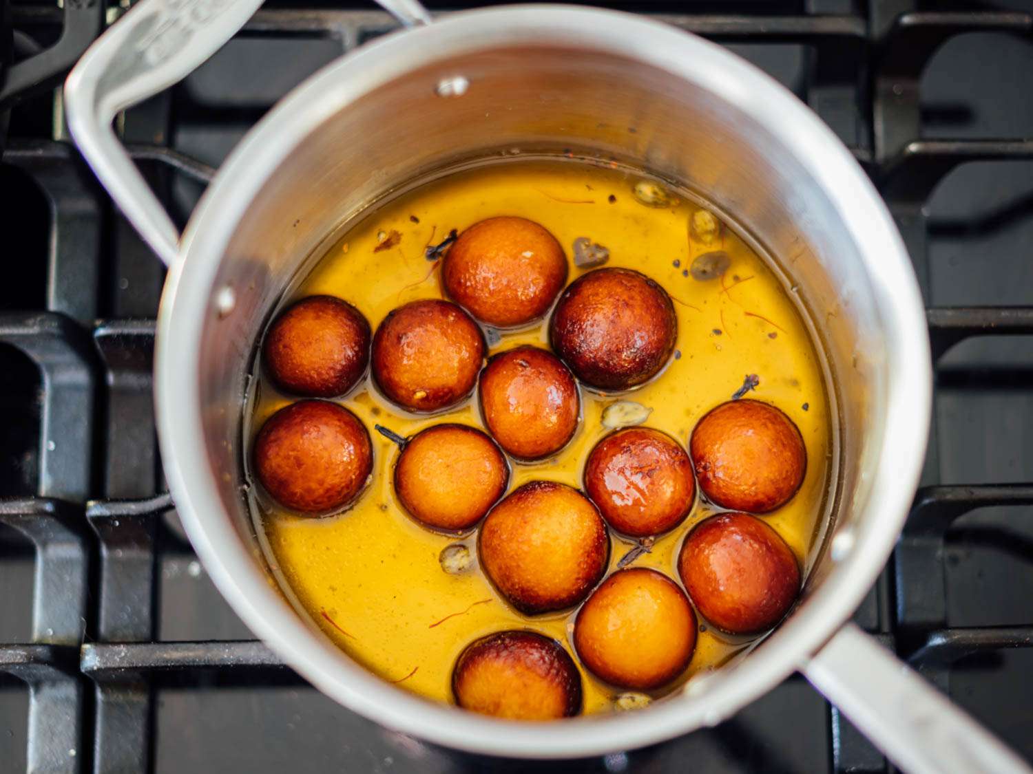 Dark brown gulab jamuns soaking in a pot of saffron-scented syrup.